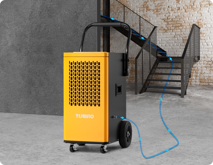 A yellow dehumidifier is positioned near a staircase, connected by a hose for moisture drainage.